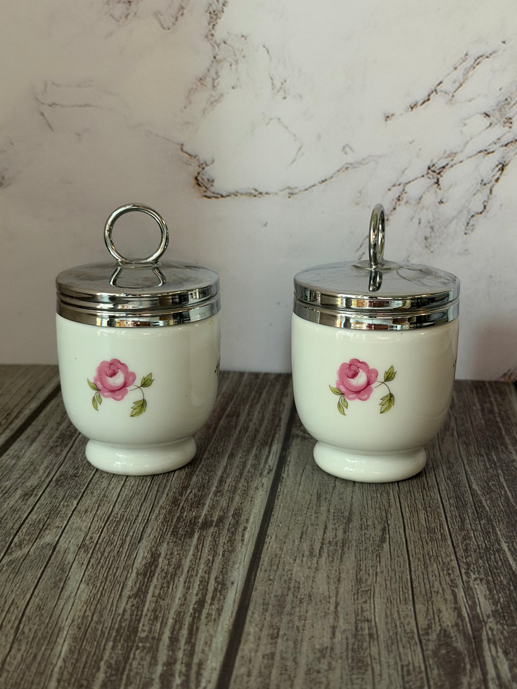 Two ceramic jars with floral designs on a wooden surface with a marble-patterned wall in the background.