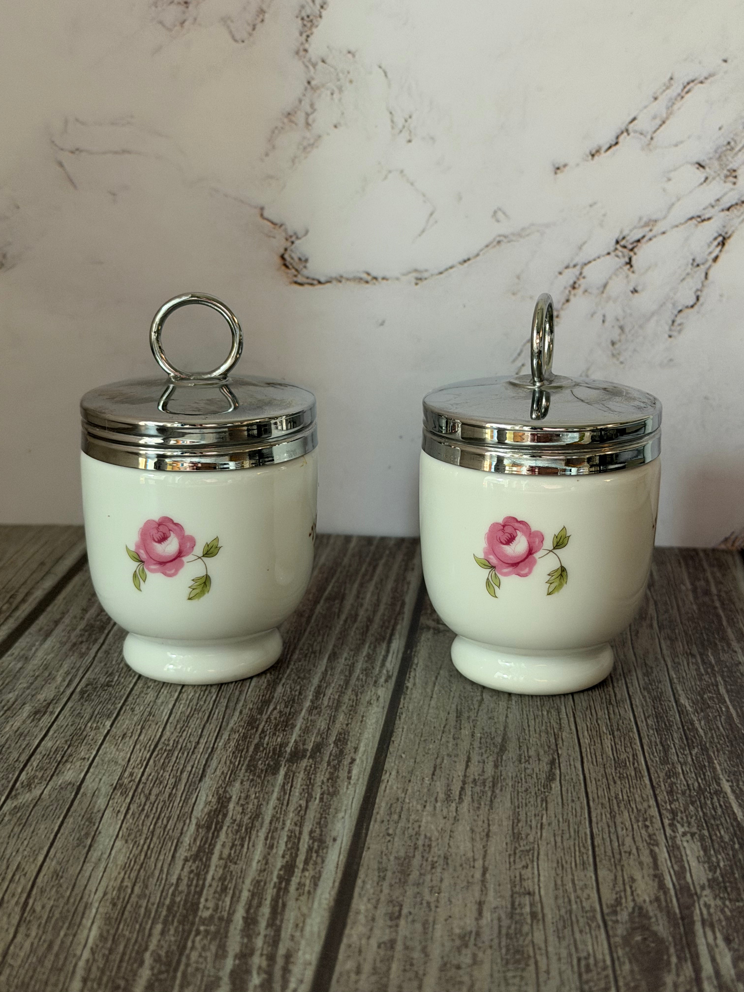 Two ceramic jars with floral designs on a wooden surface with a marble-patterned wall in the background.