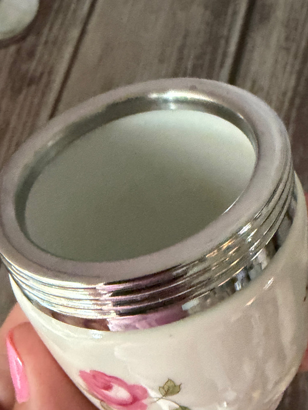 Close-up of a white container with floral design and silver lid on a wooden surface.