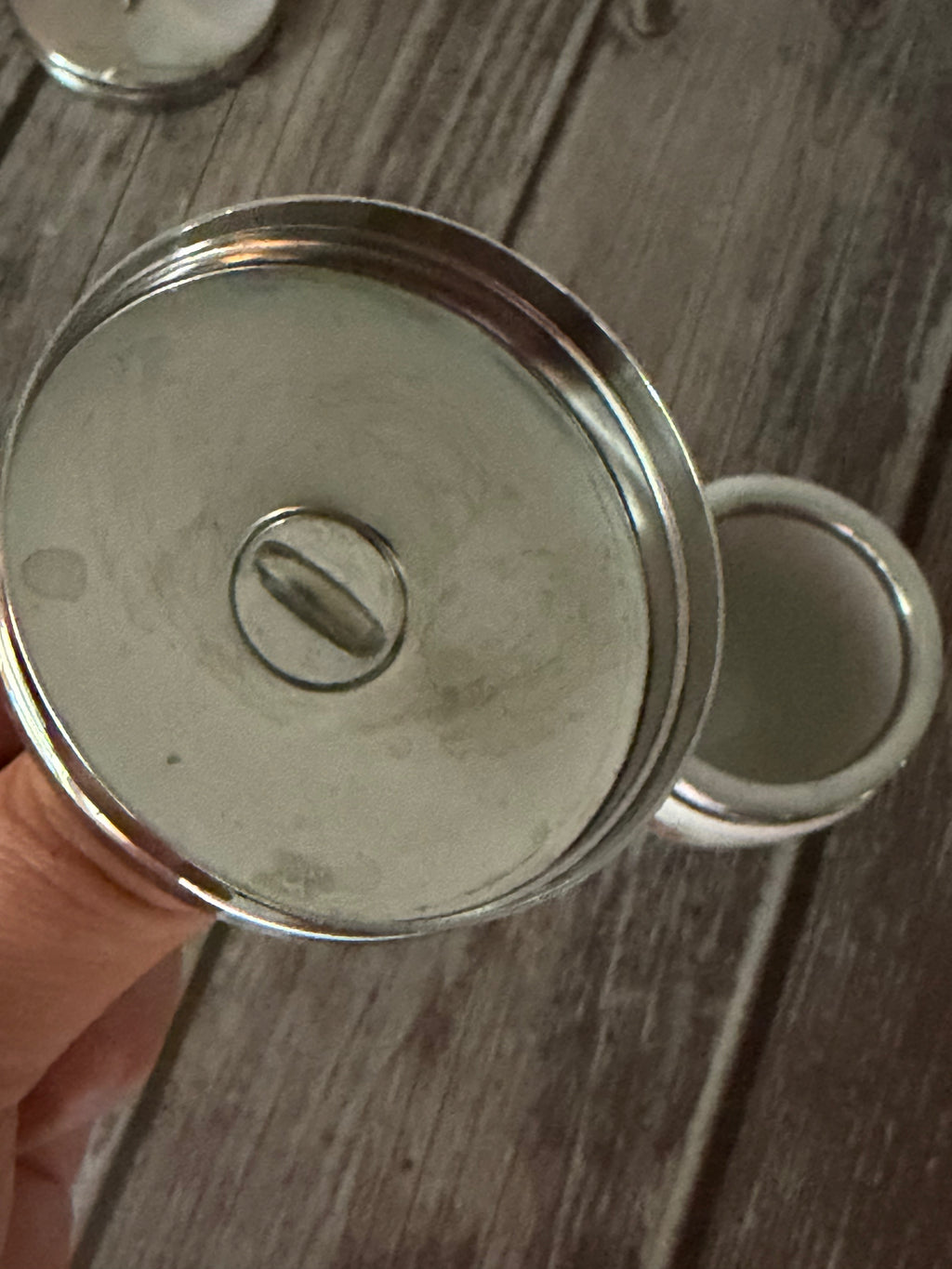 Metallic container lid held by a hand on a wooden surface