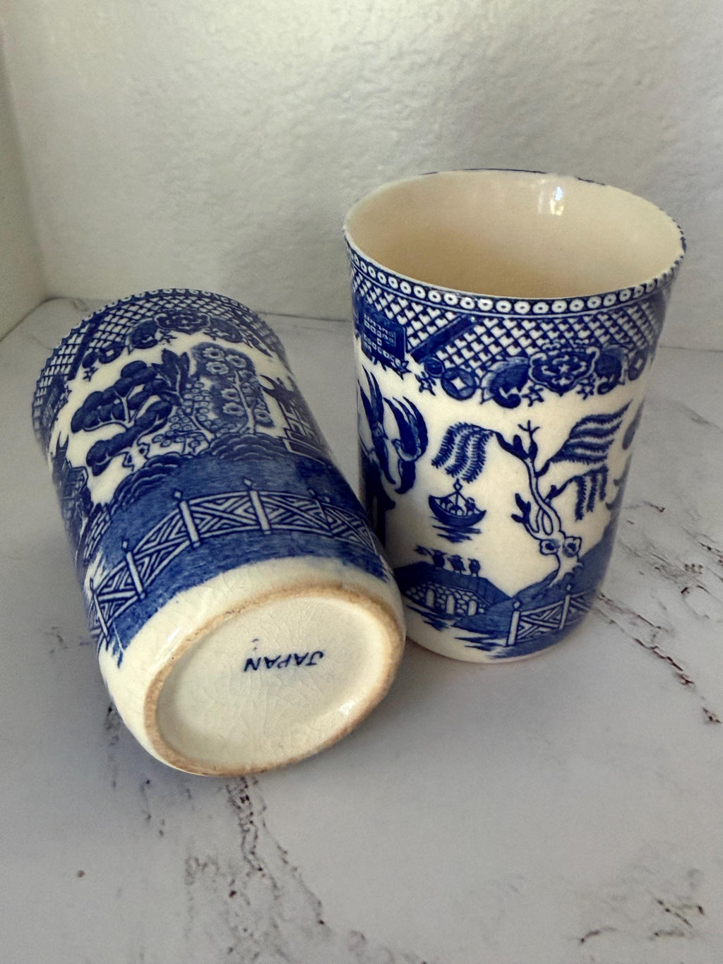 Two blue and white ceramic cups with intricate patterns on a marble surface.
